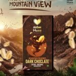 Huco Roasted Peanut Dark Chocolate bar displayed in a luxurious chocolate landscape with roasted peanuts, cocoa splashes, and premium handcrafted packaging.